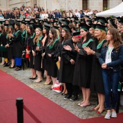 Festivitate de absolvire cu studenți și familiile acestora în fundal.