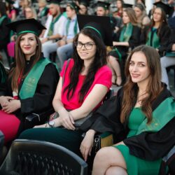 Grup de studenți absolvenți așezați pe scaune, pregătiți pentru ceremonie