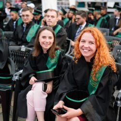 Două studente zâmbind în timpul ceremoniei de absolvire.